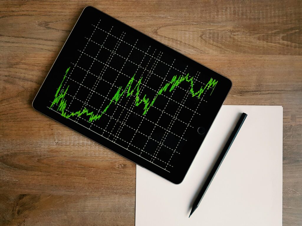 Risco e Retorno Flatlay of an iPad displaying stock market graph on a wooden desk with a pencil and paper.Risco e Retorno