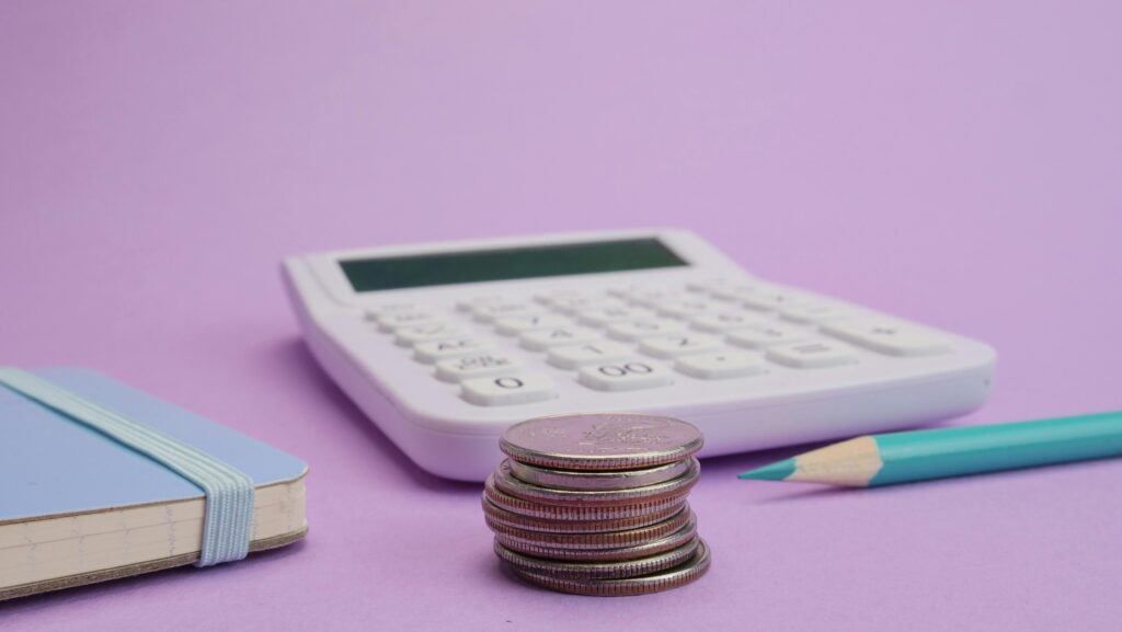 Calculator, coins, and stationery symbolize budgeting and finance on a pastel purple backdrop.