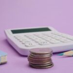 Calculator, coins, and stationery symbolize budgeting and finance on a pastel purple backdrop.