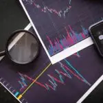Stock market charts analyzed with a magnifying glass and calculator for financial research. Ações e Obrigações