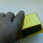 Close-up of a metal gloved hand holding a shiny gold bar indoors.