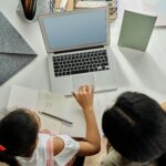 A mother helps her daughter with schoolwork on a laptop at home, promoting education and bonding.