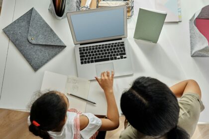 A mother helps her daughter with schoolwork on a laptop at home, promoting education and bonding.